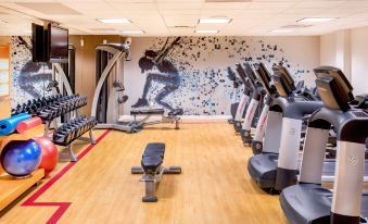 a gym with various exercise equipment , including treadmills and weight machines , under a mural of a person on the wall at Sheraton Portsmouth Harborside Hotel