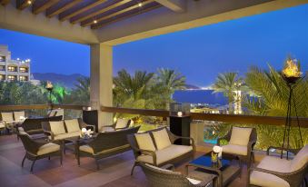 a patio area with several chairs and a dining table , surrounded by palm trees and overlooking a body of water at InterContinental Hotels Aqaba (Resort Aqaba)