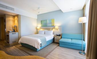 a modern hotel room with a blue bed , white bedding , and a blue couch , all lit by two lamps on either side of the bed at Holiday Inn Mauritius Mon Tresor