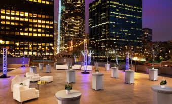 a rooftop dining area with tables and chairs , surrounded by tall buildings at night , creating a city atmosphere at The Westin Bonaventure Hotel & Suites, Los Angeles