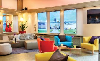 a modern living room with colorful chairs and couches , along with three large windows displaying pictures of cityscapes at Leonardo Hotel Karlsruhe