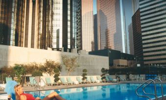 a woman in a bikini is relaxing by the edge of a pool , surrounded by tall buildings at The Westin Bonaventure Hotel & Suites, Los Angeles