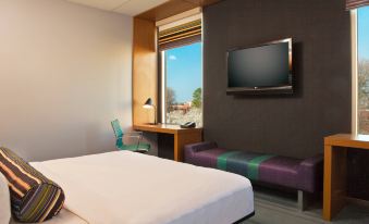 a modern hotel room with a large bed , desk , and window , along with a tv on the wall at Aloft Chesapeake