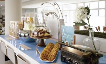 a dining table with a variety of food items , including waffles and other desserts , as well as utensils like forks and spoons at Novotel Marne la Vallee Noisy le Grand Hotel