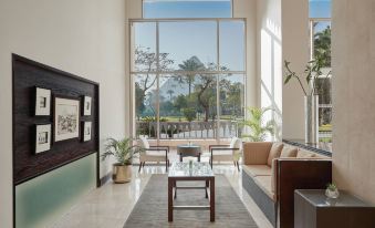 a modern living room with large windows , wooden furniture , and green plants , offering a view of the outdoors at Marriott Mena House, Cairo