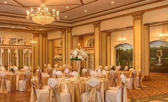 a large , elegant dining room with multiple round tables covered in gold tablecloths and surrounded by white chairs at Peabody Memphis