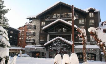 a large brown building with a stone facade and balconies is surrounded by snow - covered trees at Avenue Lodge Hotel & Spa
