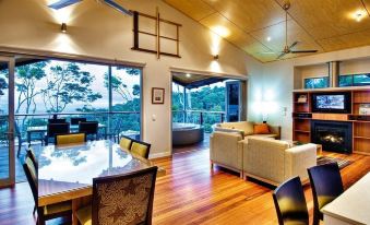 a spacious living room with wooden floors , large windows offering views of the ocean , and various furniture pieces at O'Reilly's Rainforest Retreat