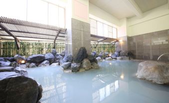 a large indoor pool filled with water , surrounded by rocks and plants , creating a serene atmosphere at Hotel Mahoroba