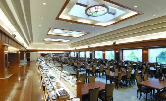 a large dining hall with wooden tables and chairs , and a long counter with various food items at Hotel Mahoroba