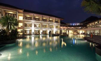 a large hotel with a swimming pool surrounded by palm trees at night , creating a picturesque scene at The Singhasari Resort Batu