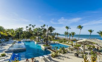 a resort with a large pool surrounded by palm trees , lounge chairs , and a beach in the background at The St. Regis Bahia Beach Resort, Puerto Rico