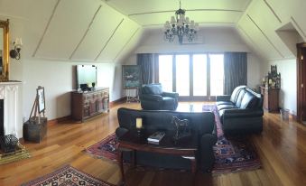 a spacious living room with hardwood floors , a large flat - screen tv mounted on the wall , and a couch placed in front of it at Lake Karapiro Lodge