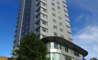 a tall , modern building with a curved design is surrounded by trees and other buildings at Park Plaza Leeds