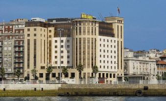 a large , multi - story building situated on the bank of a body of water in a city setting at Hotel Bahia