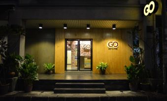 a building entrance with a large wooden door , surrounded by plants and trees , inviting customers to enter at Go Hotel