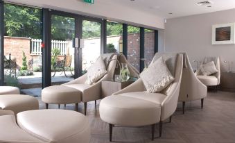 a modern living room with two white armchairs , a wooden floor , and large windows offering views of the outdoors at Macdonald Craxton Wood Hotel