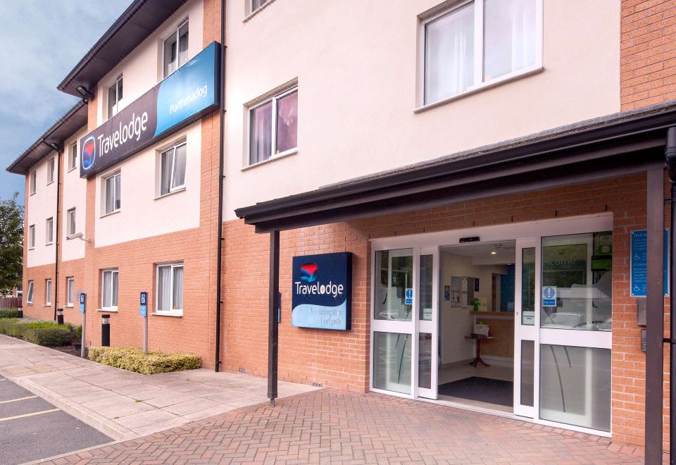 an exterior view of a travelodge hotel , featuring a brick building with multiple windows and a blue sign above the entrance at Travelodge Porthmadog