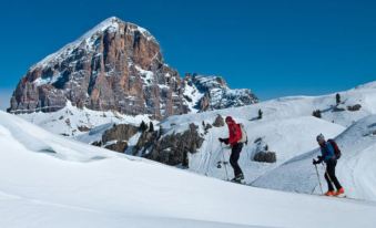 a man and a woman are cross - country skiing down a snow - covered slope , with mountains in the background at Royal Hotel Cortina