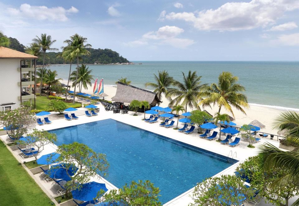 a large swimming pool with blue umbrellas and lounge chairs is surrounded by palm trees and beach chairs at Hyatt Regency Kuantan Resort