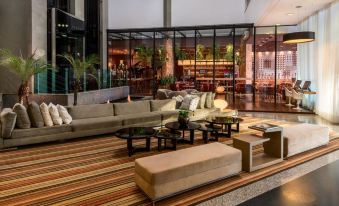 a modern living room with a couch , coffee table , and striped rug , as well as a large glass door leading to an outdoor patio at Mercure Belo Horizonte Vila da Serra
