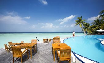 a large wooden deck overlooking a pool , with several tables and chairs set up for dining at Filitheyo Island Resort