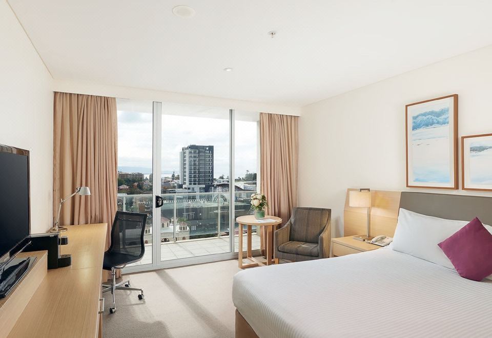 a hotel room with a large window overlooking a cityscape , featuring a comfortable bed and a desk at Sage Hotel Wollongong