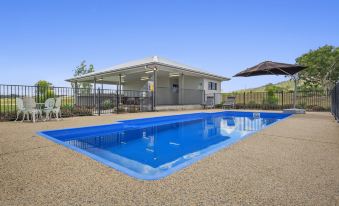 a large blue pool is surrounded by a gravel area and a covered patio with a umbrella at Casa Nostra Motel