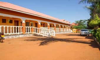 a row of orange buildings with white railings and cars parked in front , under a clear blue sky at Country Inn Masindi