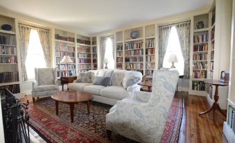 a cozy living room with a large white couch , two chairs , and a bookshelf filled with books at Woodville Bed and Breakfast