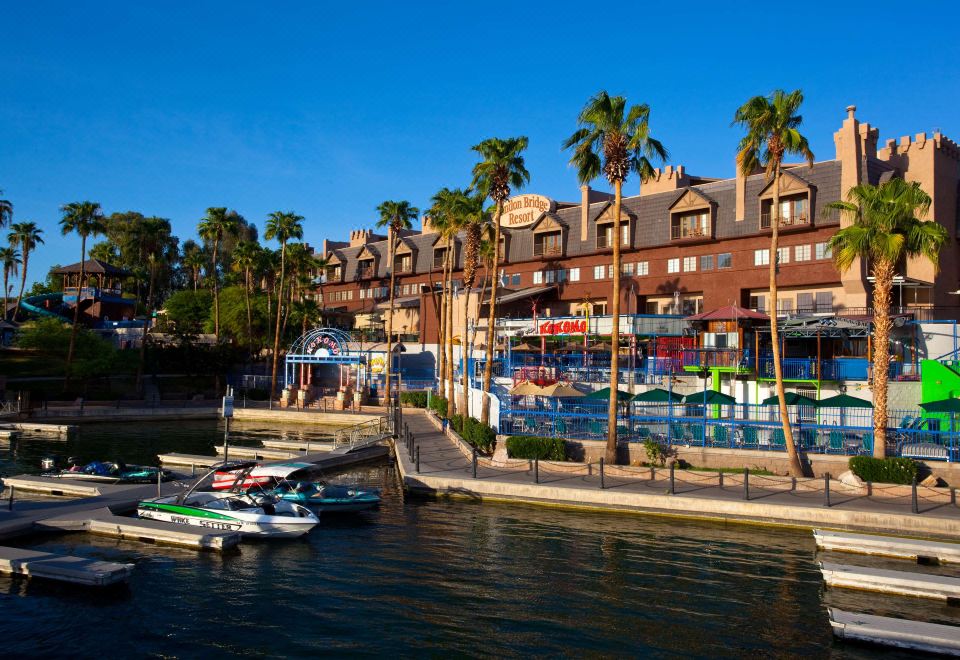a hotel surrounded by palm trees , with boats docked along the waterfront and a clear blue sky at London Bridge Resort