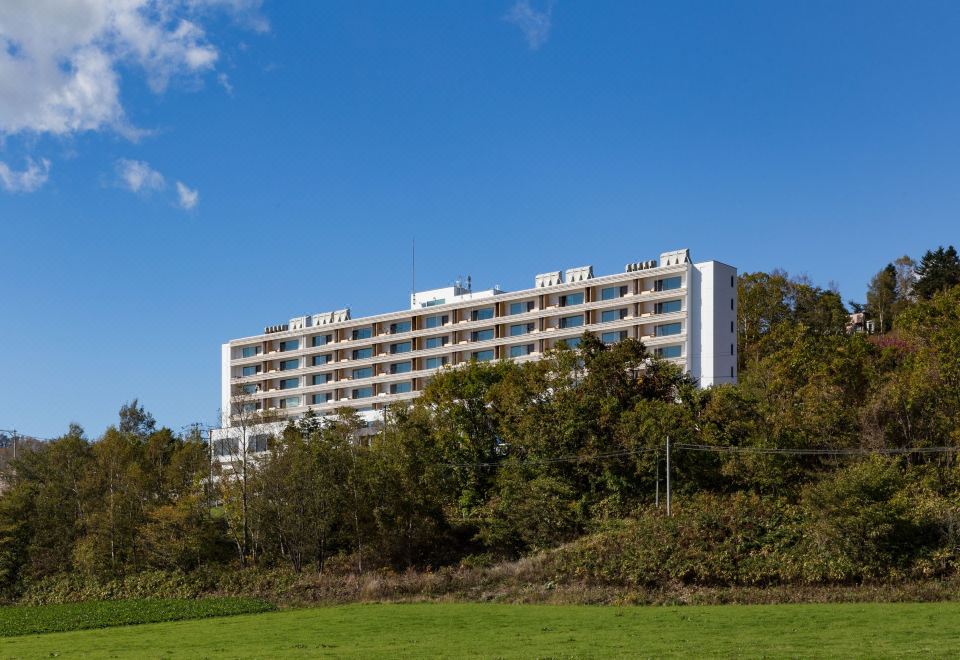 a large white building with multiple floors and balconies is surrounded by trees and grass at WE Hotel Toya