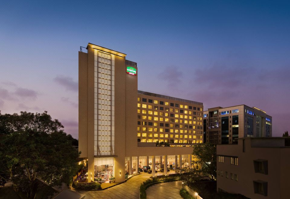 a large hotel building surrounded by trees , with the sun setting in the background at Courtyard by Marriott Mumbai International Airport