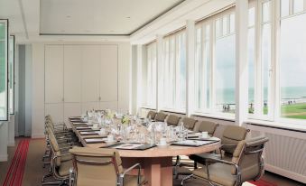 a conference room with a long wooden table , beige chairs , and multiple windows offering views of the ocean at Grand Hotel Heiligendamm - the Leading Hotels of the World