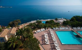 a resort with a large pool surrounded by lounge chairs and umbrellas , overlooking the ocean at Domina Zagarella Sicily