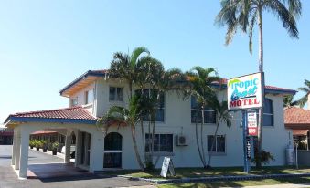 a white building with palm trees in front of it , and a sign on the side of the building at Tropic Coast Motel