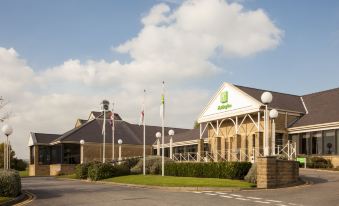 a large building with a green sign and flags is shown in the image at Holiday Inn Leeds - Brighouse