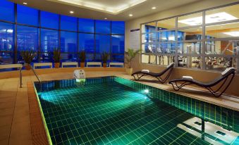 an indoor swimming pool with blue and green tiles , surrounded by lounge chairs and a large window at Sheraton Poznan Hotel