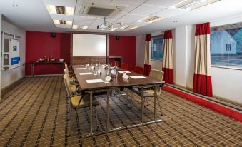 a conference room with a long wooden table , chairs , and a projector screen in the background at Holiday Inn Express Warwick - Stratford-Upon-Avon