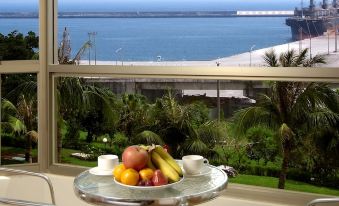a dining table with a bowl of fruit sits on it , overlooking a body of water at Ocean Hotel