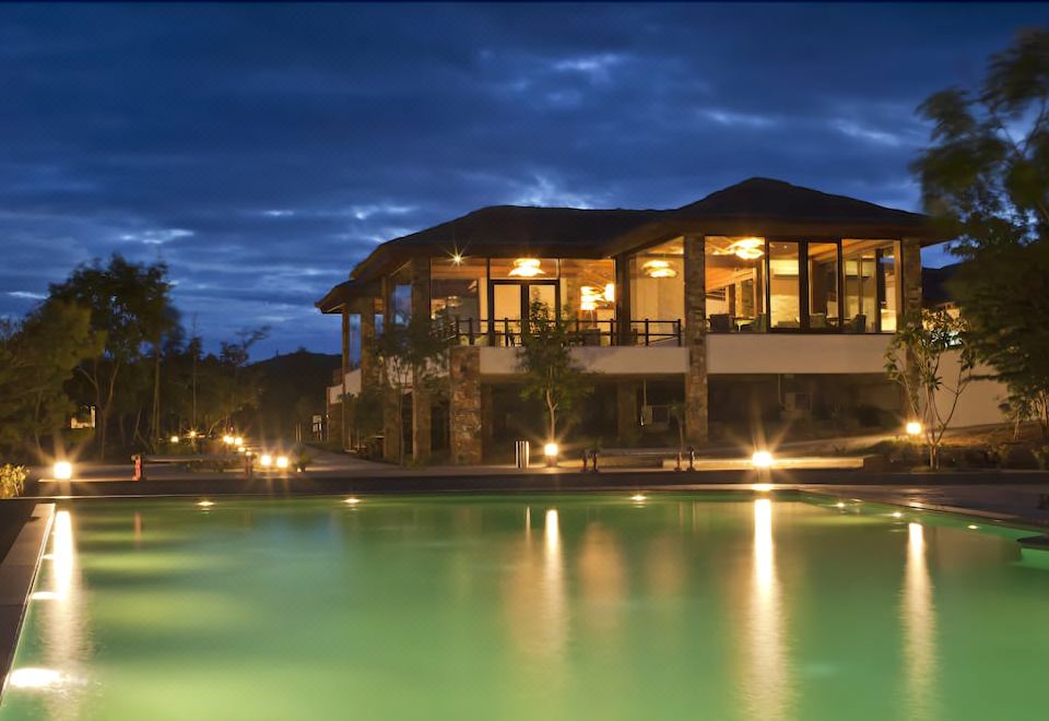 a large house with a pool in the backyard is illuminated by lights at night at The Serai Bandipur