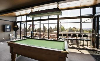 a billiards room with a pool table , surrounded by tables and chairs , and large windows offering views of the outdoors at Nightcap at Riverside Hotel