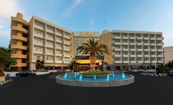 a large hotel building with a fountain in front of it , surrounded by a parking lot at GrandResort by Leonardo Hotels