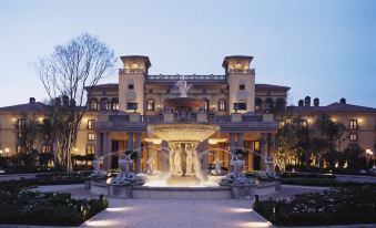 a large , luxurious hotel building with a fountain in front of it , surrounded by lush greenery at Palazzo Hotel