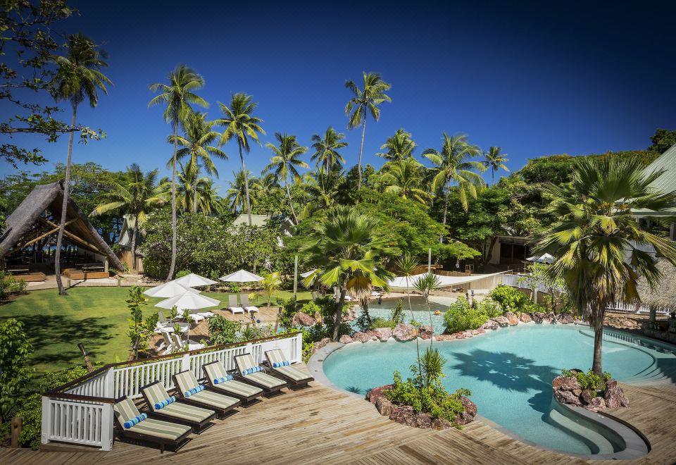 a tropical resort with a large swimming pool surrounded by palm trees , umbrellas , and sun loungers at Malolo Island Resort