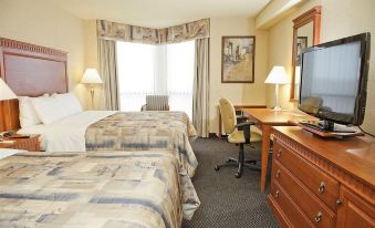 a hotel room with two beds , a desk , and a window , decorated in neutral colors at Quality Inn & Suites Bay Front
