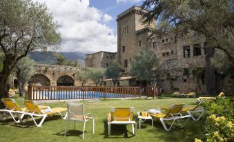 a large pool is surrounded by lounge chairs and a stone building in the background at Parador de Jarandilla
