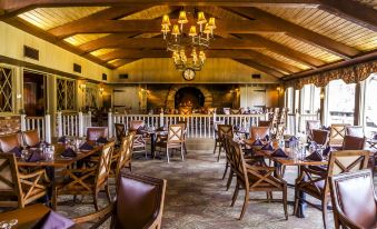 an empty restaurant with wooden chairs and tables , a fireplace , and chandeliers hanging from the ceiling at Pine Needles Lodge & Golf Club