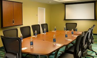 a conference room with a long wooden table surrounded by chairs , water bottles , and a projector screen at SpringHill Suites Alexandria