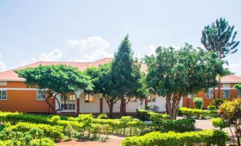 a brick building surrounded by a lush green garden , with several trees and bushes in the yard at Country Inn Masindi